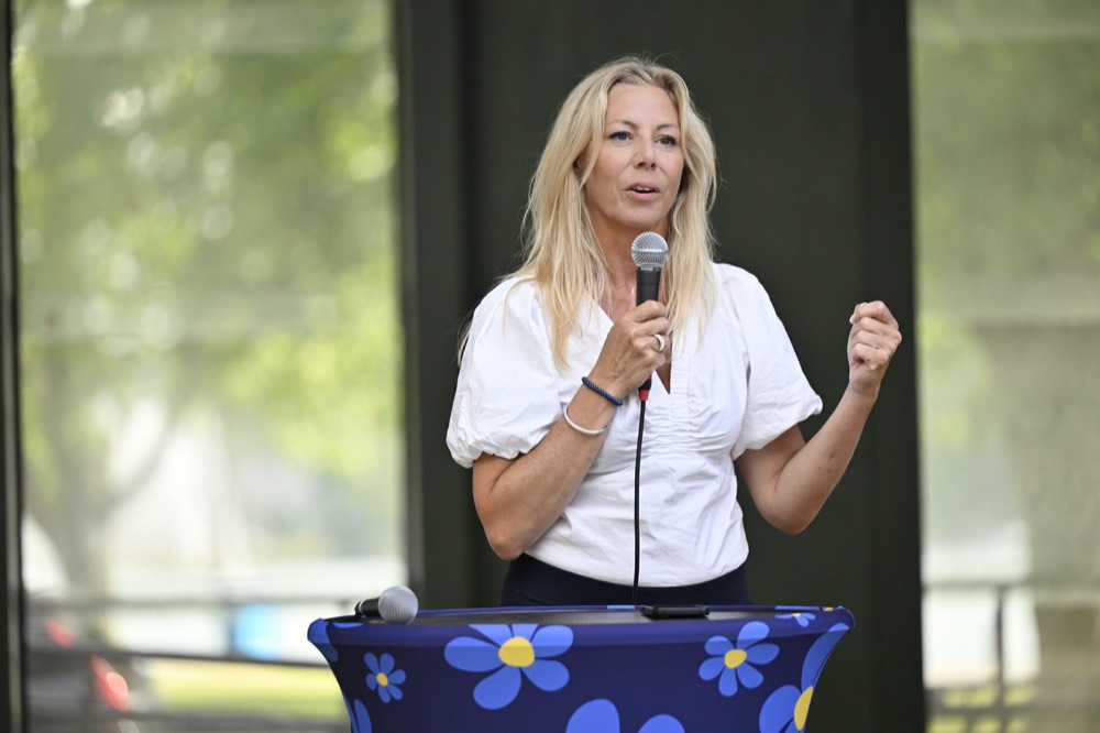 Linda Lindberg talar i mikrofon under ett utomhusarrangemang.